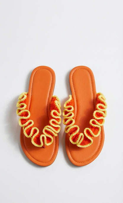 Pair of orange sandals with yellow crochet ruffled straps on white background