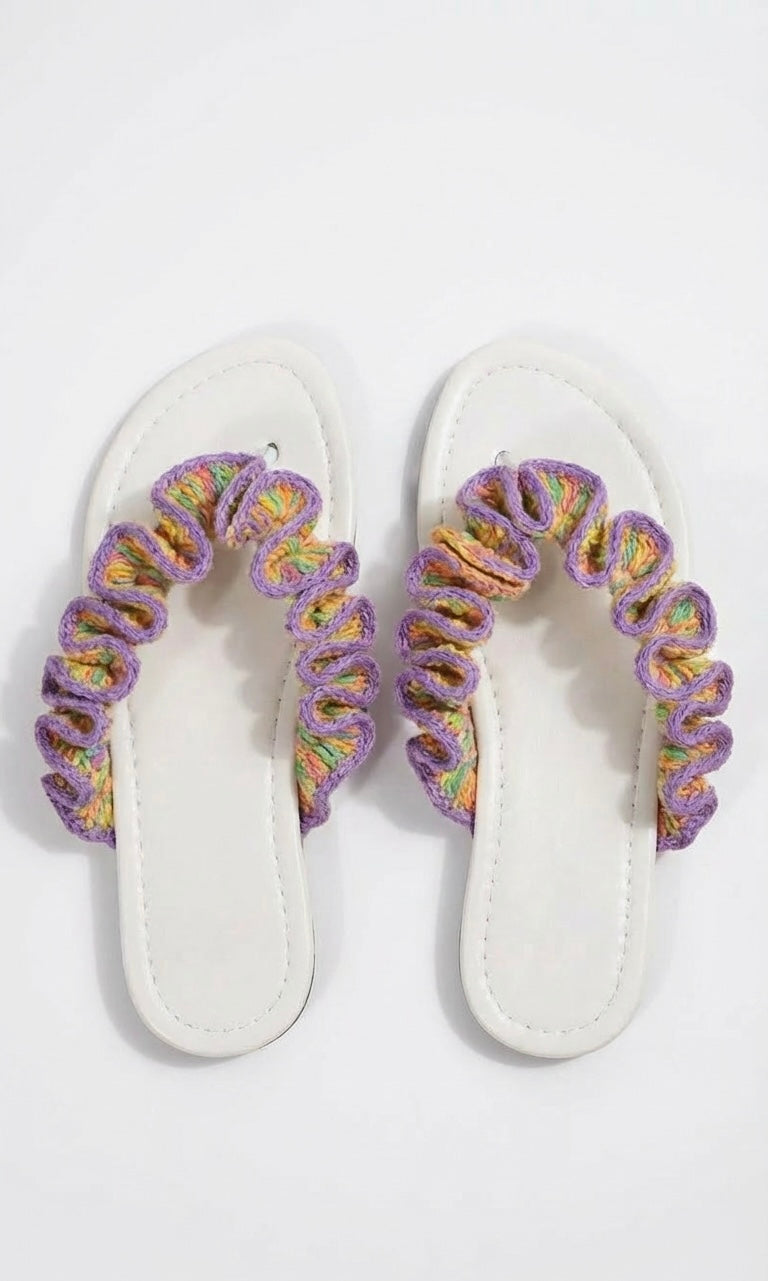 Pair of white sandals with multicoloured crochet ruffled  straps on a white background