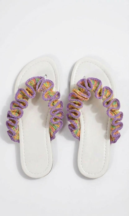 Pair of white sandals with multicoloured crochet ruffled  straps on a white background