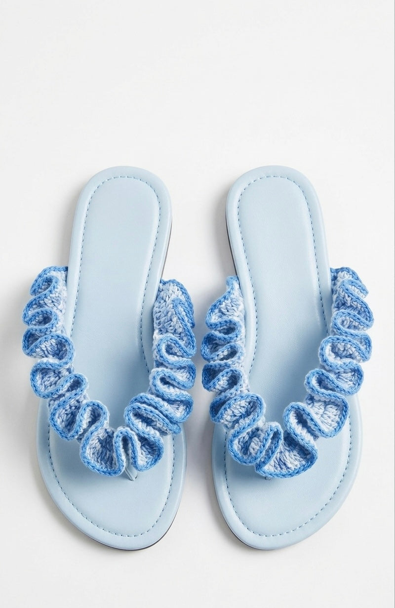 Pair of light blue sandals with crochet ruffled straps on a white background