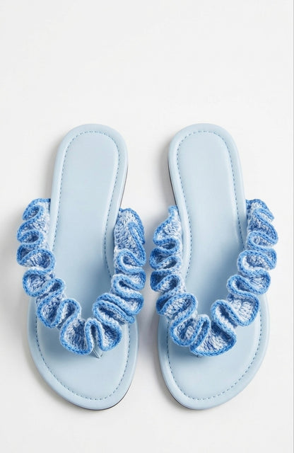 Pair of light blue sandals with crochet ruffled straps on a white background